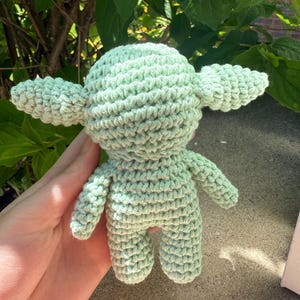 Puede incluir: Mu&ntilde;eco de ganchillo verde claro con orejas grandes y cuerpo peque&ntilde;o. El mu&ntilde;eco est&aacute; hecho a mano con una puntada texturizada, y los detalles incluyen brazos y piernas peque&ntilde;os. El mu&ntilde;eco es un personaje de una popular franquicia de ciencia ficci&oacute;n.