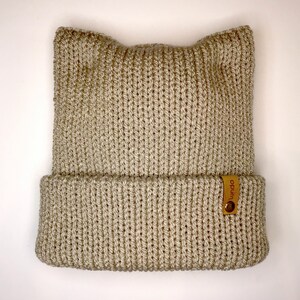 May include: A beige knitted beanie with cat ears and a brown leather label that says "Wunda".