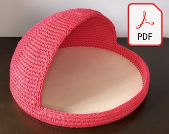 Può includere: Un letto per gatti in crochet rosa con una parte superiore arrotondata a forma di cupola e una base piatta circolare. Il letto è realizzato con un filato morbido e testurizzato e ha un aspetto accogliente e invitante.