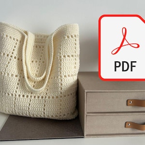 May include: A cream-coloured crochet tote bag with an openwork design. The bag has two handles and is on a grey surface. A PDF icon with a red border is visible on the right, next to a two-drawer storage box.