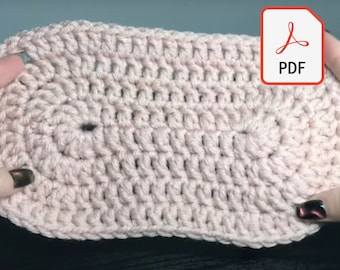May include: A close-up of a pink crocheted oval. The oval is made with a simple stitch pattern and has a hole in the center.