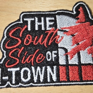 以下が含まれることがあります： 「THE South Side OF H-TOWN」の文字が刺繍されたパッチ。パッチは、白と赤の文字と赤いグラフィックが入った黒い背景が特徴です。パッチは、白いステッチの黒い縁取りが施されています。