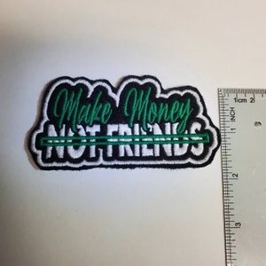 May include: Black and white embroidered patch with green lettering that reads "Make Money Not Friends". The patch is approximately 2 inches wide.