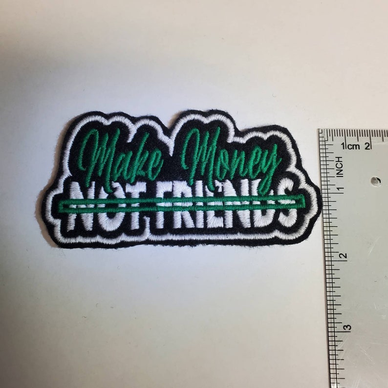 May include: Black and white embroidered patch with green lettering that reads "Make Money Not Friends". The patch is approximately 2 inches wide.