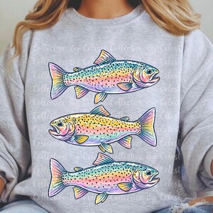 May include: A light gray sweatshirt featuring three colorful rainbow trout illustrations. Each fish is detailed with vibrant hues of yellow, pink, blue, and green. The design is repeated across the sweatshirt.