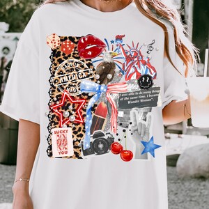 May include: White t-shirt featuring a collage of patriotic and pop culture elements. Includes a red star, dice, lips, an eagle, the Statue of Liberty, and the text "MADE IN AMERICA". Also features the text "LUCKY YOU" and "I was able to do many things at the same time, I became Wonder Woman".