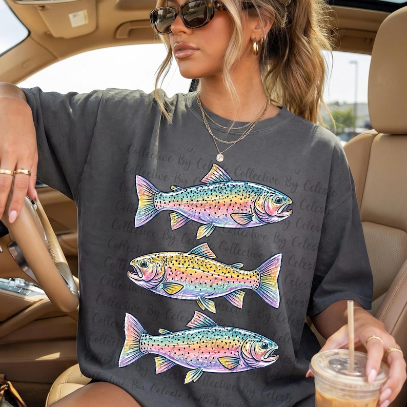 May include: Dark grey t-shirt featuring three colorful fish illustrations. The fish have rainbow-colored scales and fins, with a detailed design. The shirt has the text "Collective By Celeste" repeated across the design.