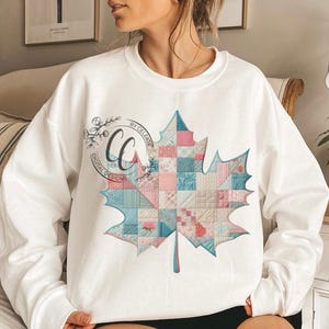 May include: White sweatshirt featuring a large, colorful maple leaf design. The leaf is composed of patchwork squares in shades of pink, blue, and cream. The text "CC DIGITAL DESIGNS BY CELESTE" is printed on the left side of the sweatshirt.