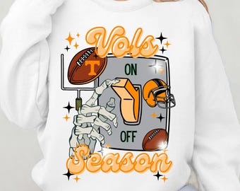 May include: White sweatshirt featuring a graphic design of a skeleton hand flipping a switch labelled "ON" and "OFF". The switch is surrounded by footballs and the text "Vols Season".