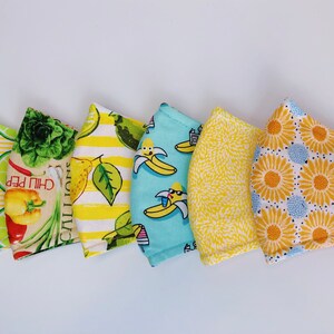May include: Five different fabric face masks with various patterns. The masks are yellow, blue, and white with designs of lemons, vegetables, bananas, flowers, and a geometric pattern.