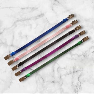 May include: Five colourful lanyards with metal clips and round button accents. The lanyards are in blue, pink, black, purple, and green. The background has a marble pattern.