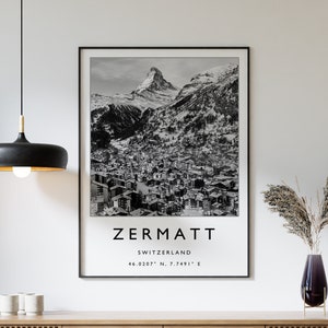Könnte beinhalten: Schwarzweißfoto des Matterhorns in Zermatt, Schweiz. Das Bild zeigt den Gipfel des Berges und die Stadt darunter. Der Text "Zermatt, Schweiz 46.0207° N, 7.7491° E" ist unter dem Bild gedruckt.