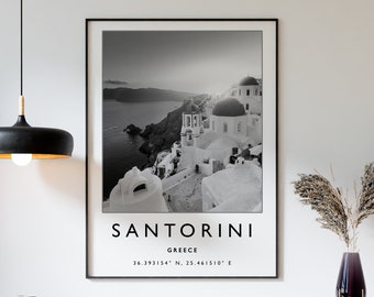 May include: A framed black and white print of Santorini, Greece, hangs above a wooden cabinet. The print features the word "SANTORINI" and coordinates. A black pendant light and a vase with dried plants are also visible.