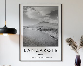 Pode incluir: Uma fotografia a preto e branco de uma paisagem costeira com uma montanha no fundo. A fotografia é enquadrada a preto e tem o texto "Lanzarote, Espanha, 29.035000° N, 13.633000° W" impresso abaixo da imagem.