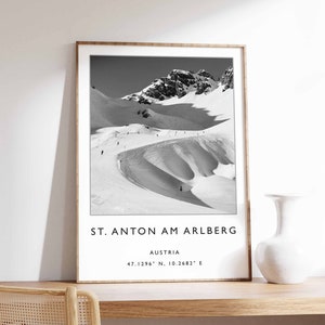 May include: Black and white photograph of snow-covered mountains with skiers on the slopes. The image is framed and includes the text "St. Anton am Arlberg, Austria, 47.1296° N, 10.2682° E".