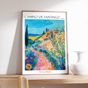 May include: A vintage travel poster featuring a colorful landscape with a winding road leading up a hill. The poster is titled "Camino de Santiago, Spain" and includes the text "The Travel Collection".