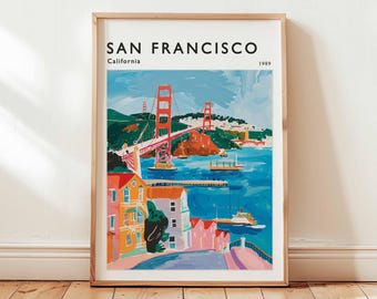 May include: A framed art print of San Francisco, California, featuring the Golden Gate Bridge in red, spanning across blue water. The print includes colorful buildings and the text "SAN FRANCISCO" and "1989". The artwork is in a wooden frame.