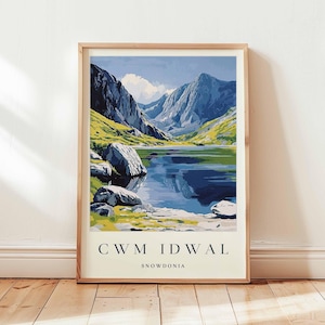 May include: A framed print depicting a mountain lake scene. The artwork is in a vintage travel poster style, with the text "CWM IDWAL SNOWDONIA" at the bottom. The color scheme includes blues, greens, and beige tones, evoking a sense of nostalgia.
