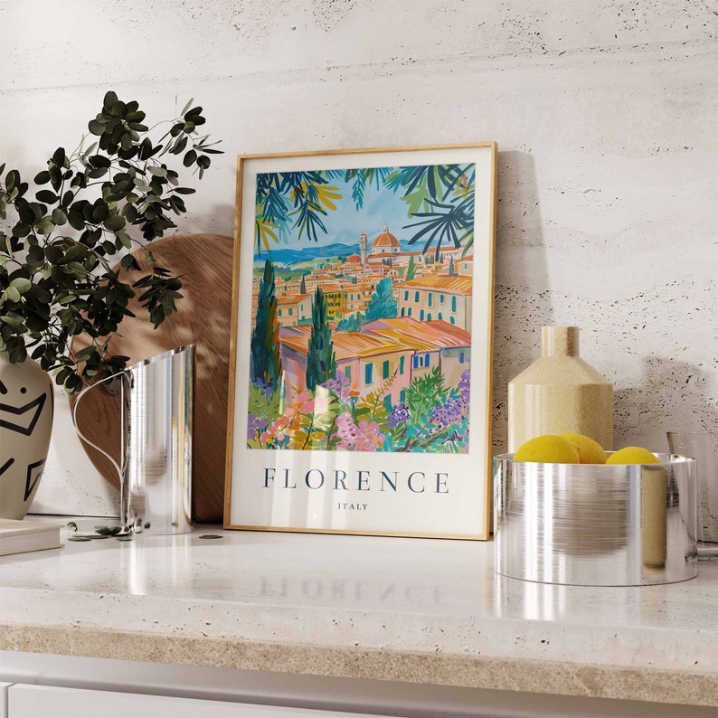 K&ouml;nnte beinhalten: Ein gerahmter Druck einer farbenfrohen Illustration von Florenz, Italien. Der Druck zeigt eine Stadtlandschaft mit Geb&auml;uden, B&auml;umen und einer Kirche. Der Text "FLORENCE ITALY" ist unter der Illustration gedruckt.