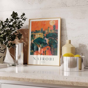 May include: A framed art print featuring a vibrant illustration of Nairobi, Kenya, with a cityscape under a sunset sky. The print includes the city's name and country. The artwork is displayed on a countertop with decorative items.