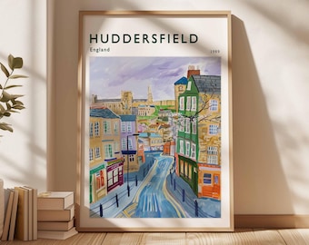 May include: A framed art print of Huddersfield, England, from 1989. The watercolor painting depicts a street scene with colorful buildings, a winding road, and a church in the background. The print is in a light wood frame.