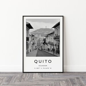 May include: Black and white photograph of a street in Quito, Ecuador. The street is lined with buildings and there are people walking on the sidewalk. The text "QUITO" is printed below the image, along with the coordinates "0.1807&deg; S, 78.4678&deg; W".