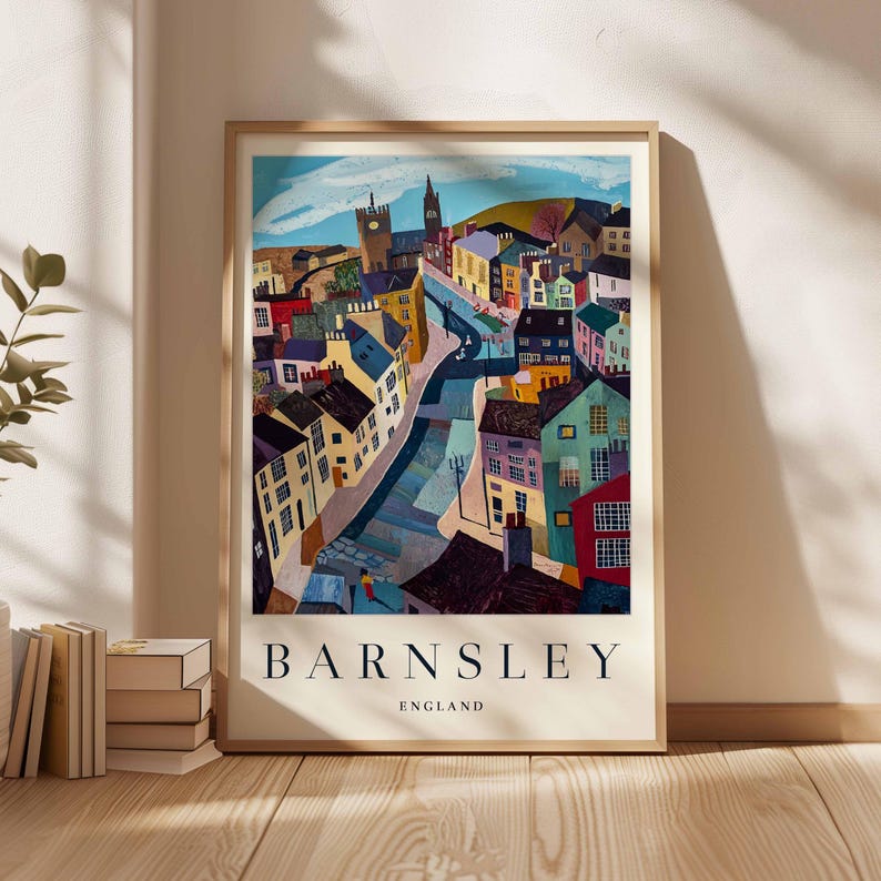Puede incluir: Una impresi&oacute;n art&iacute;stica enmarcada que presenta una representaci&oacute;n colorida y estilizada de Barnsley, Inglaterra. La obra de arte muestra un paisaje urbano con edificios de varios colores, una carretera central y una torre de iglesia. Las palabras "BARNSLEY" y "ENGLAND" est&aacute;n impresas en la parte inferior.