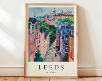 May include: A framed art print of Leeds, England, featuring a colorful street scene with buildings in shades of pink, blue, and orange. The print has the word "LEEDS" and "ENGLAND" printed in a serif font at the bottom.