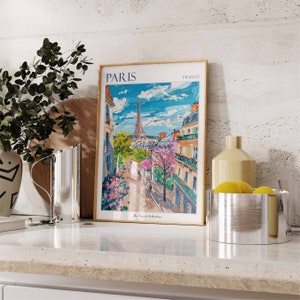 May include: A framed print of a colorful painting depicting a Parisian street scene with the Eiffel Tower in the background. The print has the text "PARIS FRANCE" at the top and "The Travel Collection" at the bottom.