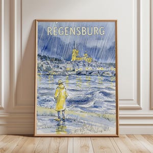 May include: A framed watercolor print titled REGENSBURG featuring a person in a yellow raincoat standing by a river during a rainstorm. The scene depicts a city skyline with a cathedral and a stone bridge under a dark, rainy sky with blue tones.