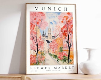 May include: A framed art print depicting a Munich street scene with a flower market. The watercolour illustration shows pink and orange trees, buildings, and the text "MUNICH FLOWER MARKET JUNE 15 WORLD IN BLOOM NO. 7".