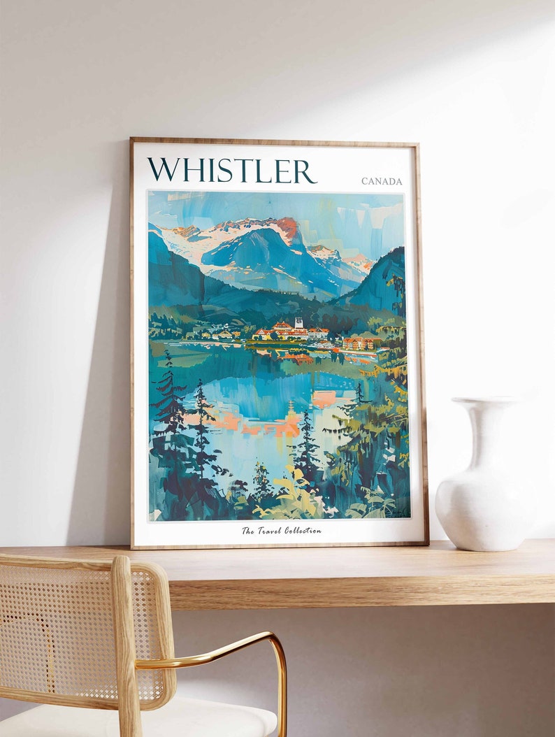May include: A vintage travel poster featuring a scenic view of Whistler, Canada. The poster depicts a mountain range with snow-capped peaks, a lake reflecting the mountains, and a small town nestled in the valley. The text "WHISTLER" and "CANADA" is printed in a bold, sans-serif font at the top of the poster. The poster is framed in a simple wooden frame.