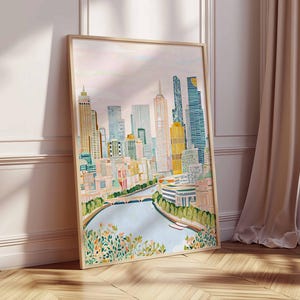 May include: A framed watercolour print of a cityscape, depicting a skyline with high-rise buildings in yellow, blue, and green hues. A river flows in the foreground, with a bridge and floral details. The frame is light wood.
