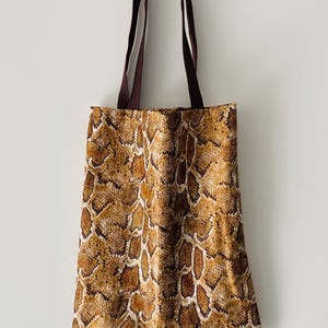 Peut inclure: Un sac cabas brun avec un motif peau de serpent. Le sac a des anses brunes.