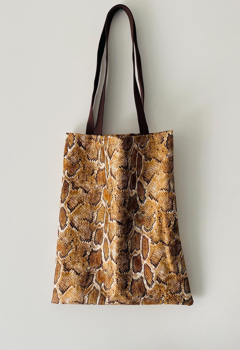 May include: A brown tote bag with a snakeskin pattern. The bag has brown straps.