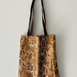 May include: A brown tote bag with a snakeskin pattern. The bag has brown straps.