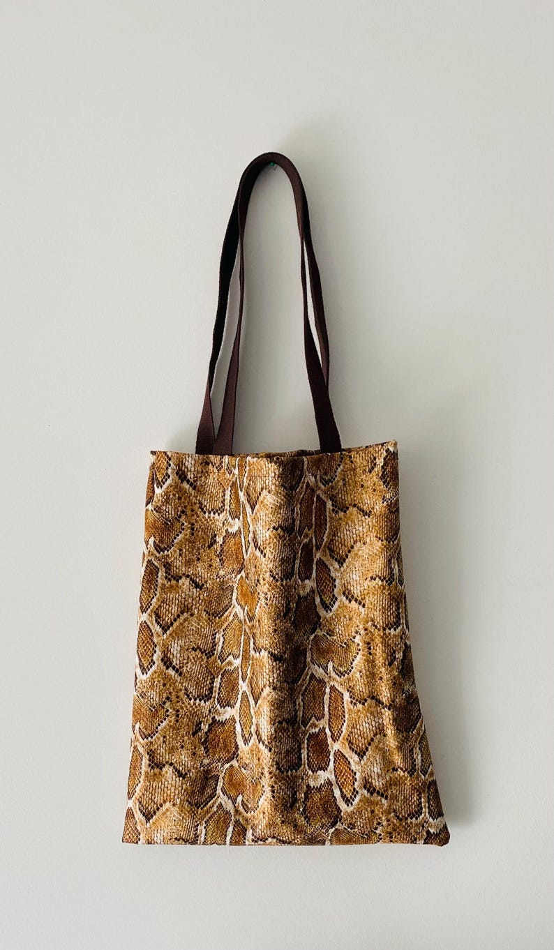 May include: A brown tote bag with a snakeskin pattern. The bag has brown straps.