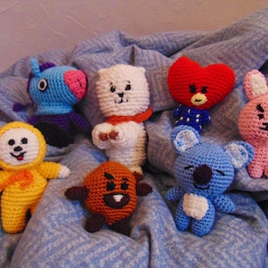 May include: Seven crocheted stuffed toys in various colors and designs, including a yellow dog, a blue unicorn, a white bear, a red heart, a pink bunny, a brown bear, and a blue koala.