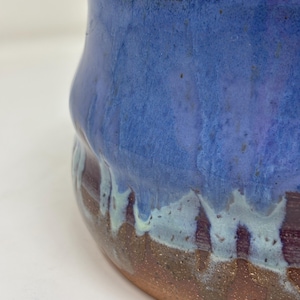 Könnte beinhalten: Ein handgefertigter Keramiktopf mit einer blauen Glasur, die nach unten tropft und eine braune Basis freilegt. Der Topf hat eine einzigartige, organische Form und ein glänzendes Finish. Der Innenraum ist dunkelbraun.