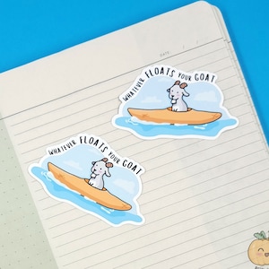 May include: Two stickers on a notebook. Each sticker features a cartoon goat in a kayak with the text "WHATEVER FLOATS YOUR GOAT". The goat is white with a small horn. The kayak is orange, and the water is blue.