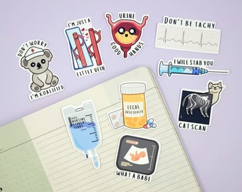 May include: A selection of medical-themed stickers on a notebook. The stickers feature humorous illustrations and text, including a koala in a nurse's hat, a vein, a bladder, an EKG, a syringe, a cat scan, an IV bag, a pill bottle, and an ultrasound image.