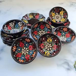 Pode incluir: Conjunto de 10 tigelas de cerâmica turca com desenhos florais coloridos. As tigelas são pretas com padrões florais brancos, vermelhos, azuis, verdes e amarelos. As tigelas são perfeitas para servir petiscos, molhos ou sobremesas.