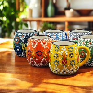 May include: Set of eight colorful ceramic mugs with intricate floral designs. Each mug features a different color and pattern, including blue, green, yellow, orange, and red.