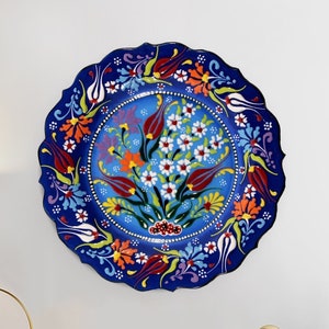 May include: A decorative ceramic plate with a scalloped edge, featuring a vibrant floral design. The plate's deep blue background is adorned with colorful flowers in red, orange, white, and green. The plate is a decorative piece for the home.