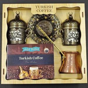 Może przedstawiać: Drewniane pudełko zawierające niezbędne elementy do kawy po turecku. Zawiera dwa ozdobne mosiężne filiżanki do kawy, dekoracyjny spodek, mosiężną łyżeczkę, miedziany dzbanek do kawy i pudełko kawy po turecku. Pudełko jest oznaczone "Turkish Coffee".