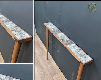 May include: A wooden console table with a top made of decorative tiles. The table has a light brown finish and features two slender legs.