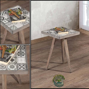 Puede incluir: Una pequeña mesa auxiliar de madera gris con tres patas. La superficie de la mesa está decorada con un diseño de azulejos de patrón blanco y negro. La mesa está sobre un suelo de madera.