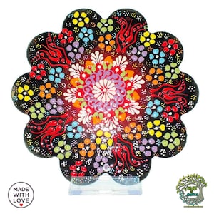 Pode incluir: Um prato de cerâmica preto em forma de flor com um design floral colorido. O prato apresenta um padrão central de branco, vermelho, roxo e laranja, rodeado por pequenos pontos amarelos, azuis e verdes. O texto "MADE WITH LOVE" é visível.