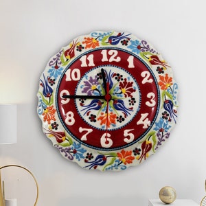 May include: A red and white ceramic wall clock with a floral design and black hands. The clock face has the numbers 1 through 12 around the edge.