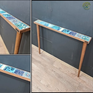 Puede incluir: Una mesa consola de madera con una tapa de mosaico de azulejos azules y verdes. La mesa tiene cuatro patas y mide aproximadamente 76 cm de alto.